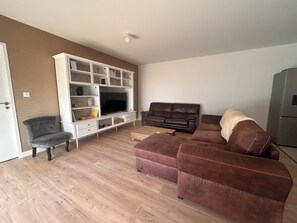 Ein Wohnzimmer mit Fernseher, zwei Sofas, einem Sessel und einer weißen Unterhaltungseinheit.