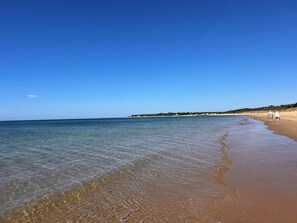 Ein Strand mit klarem Wasser, sandigem Ufer und einigen Spaziergängern.