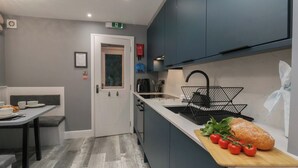 Une cuisine moderne dotée d’un îlot central intégré, d’un évier avec un robinet noir et d’une planche à découper en bois sur laquelle on voit des tomates et une miche de pain.