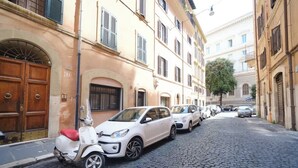 Een geplaveid straatje omzoomd door historische gebouwen, geparkeerde auto's en een scooter.