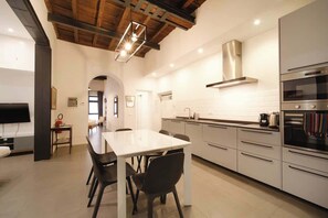 A modern kitchen with a dining area, stainless steel appliances, and a wooden ceiling. - BuddyRent - Golden House - Patio - Monti - 7 (Roma)