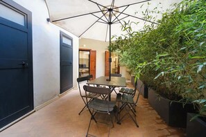 An outdoor patio with a table and chairs, a large umbrella, and a potted plant.