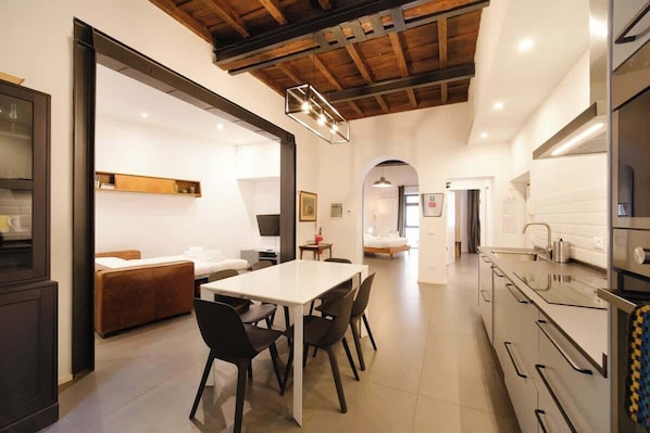 A modern kitchen with a dining area, wooden ceiling beams, and a large window.