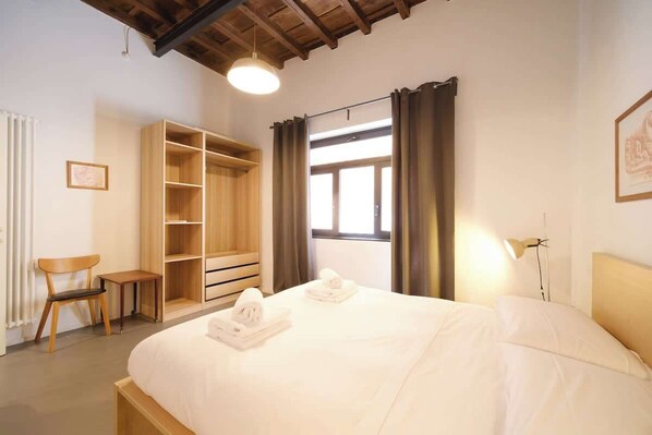 A bedroom with a bed, a wooden wardrobe, a chair, and a bedside table.