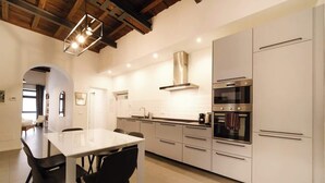 Een moderne keuken met witte kasten, een roestvrijstalen oven, en een eethoek met een witte tafel en zwarte stoelen.