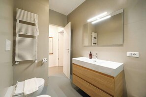 A modern bathroom with a white sink, wooden vanity, and a large mirror.