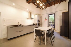 A modern kitchen with a white countertop, grey cabinets, a stainless steel range hood, and a dining area with a white table and black chairs.