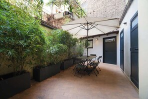 A patio with a table and chairs, surrounded by potted plants and a large umbrella.