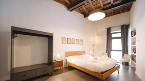 Een slaapkamer met een bed, nachtkastjes, een kledingkast, een leeshoek, een boekenkast en een raam met gordijnen.