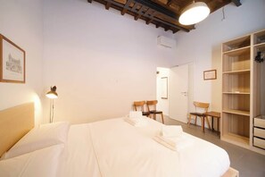 A bedroom with a bed, a desk, two chairs, a wardrobe, and a framed picture on the wall.