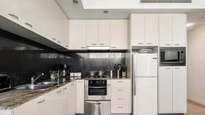 Una cocina moderna con armarios blancos, electrodomésticos de acero inoxidable, encimera de mármol y salpicadero negro.