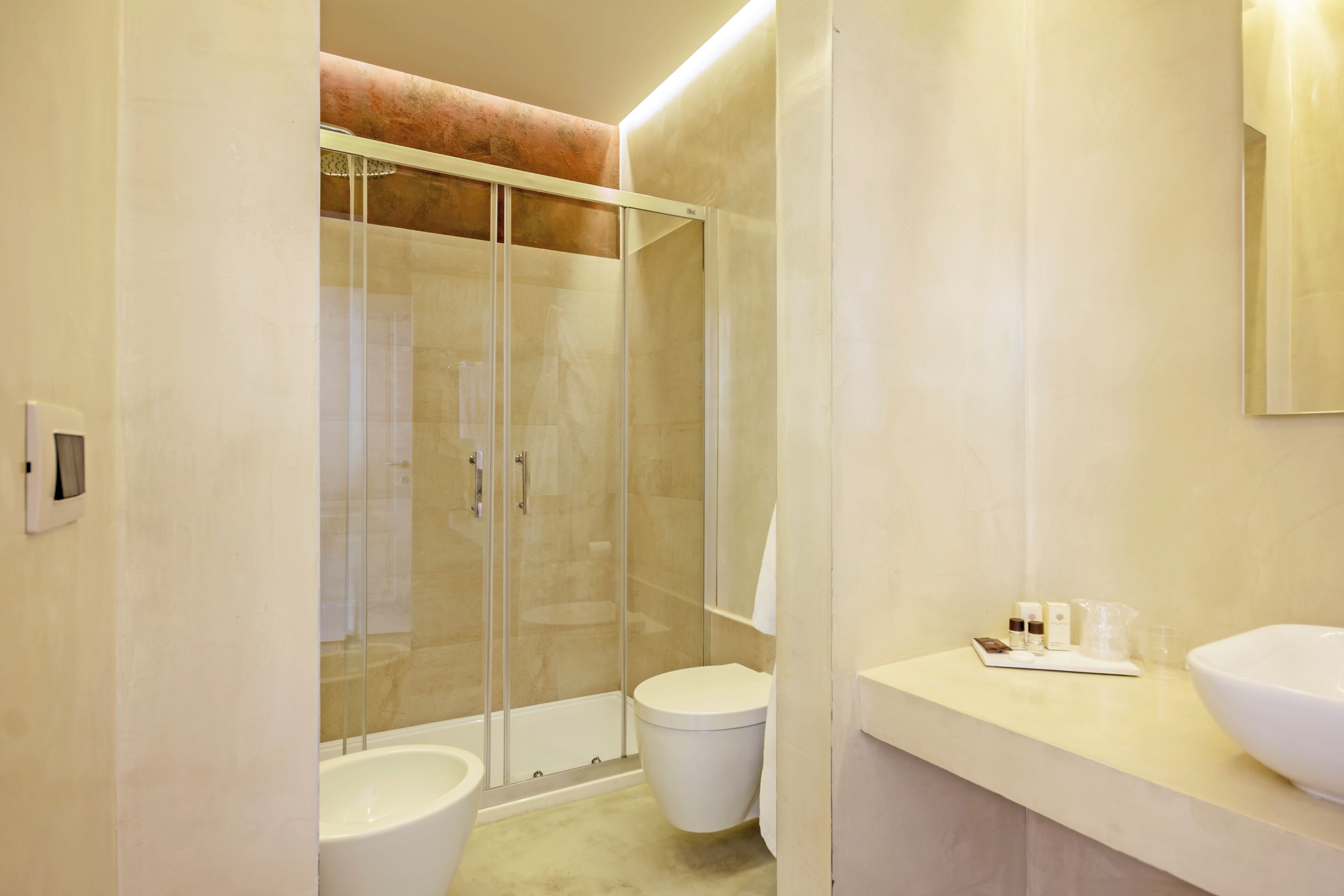 Een moderne badkamer met een douchecabine van glas, een wit toilet en een wastafel met toiletartikelen.