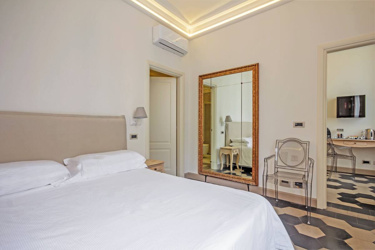 A hotel room with a large bed, a mirror, a desk, and a chair.