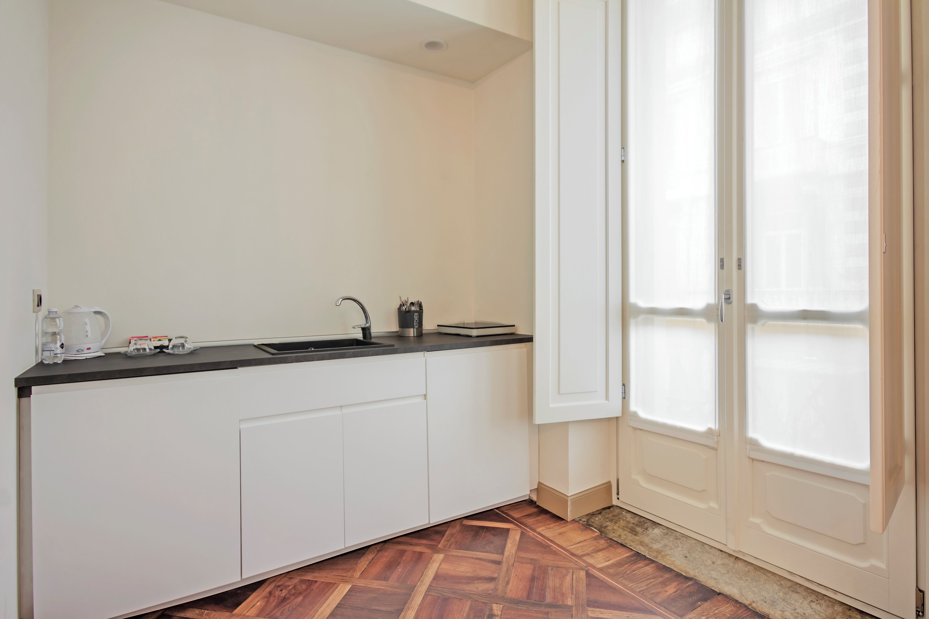 Una cocina con armarios blancos, encimera negra y ventana con vidrio esmerilado.