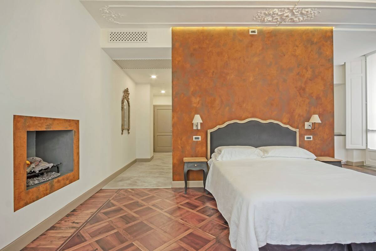 A bedroom with a large bed, a fireplace, and a decorative wall panel.