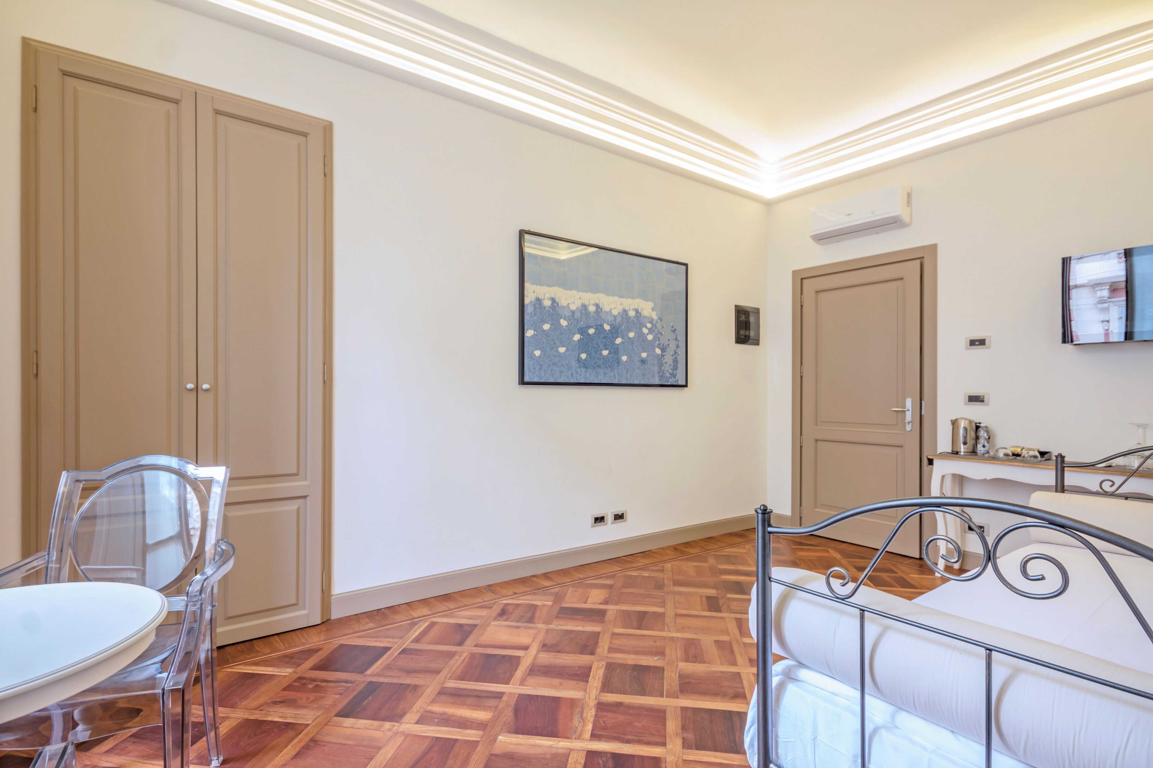 Una camera d'albergo con pavimento in parquet di legno, un letto con struttura in metallo, un tavolo da pranzo con sedie e un quadro appeso al muro.
