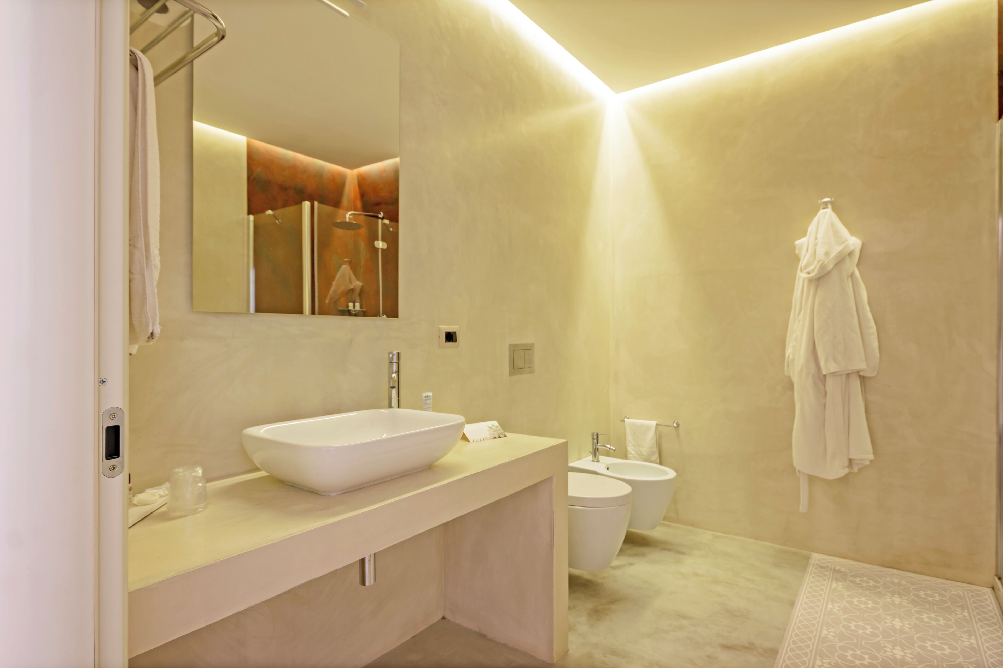 A modern bathroom with a large sink, a toilet, and a bidet. There is a towel hanging on the wall and a mirror above the sink.