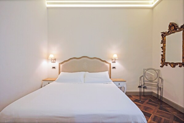 A neatly made bed with a wooden headboard, two bedside tables with lamps, a chair, and a mirror on the wall. - SUYTE Torino Centro (Turin)
