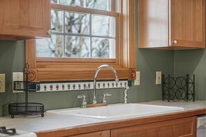 Una cocina con armarios de madera, un lavamanos blanco y una ventana con vistas a árboles.