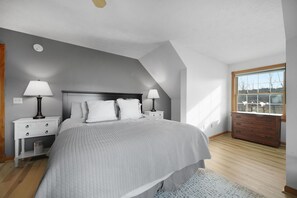 Un dormitorio con una cama grande, dos mesitas de noche con lámparas, un aparador y una ventana con vistas.