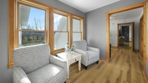 Une pièce avec une grande fenêtre, un canapé, une petite table sur laquelle sont posées des bouteilles en verre, et un plancher en bois.