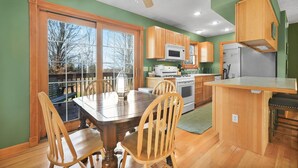 Une cuisine avec des meubles de rangement en bois, une table à manger avec des chaises et une vue dégagée grâce à de grandes fenêtres.