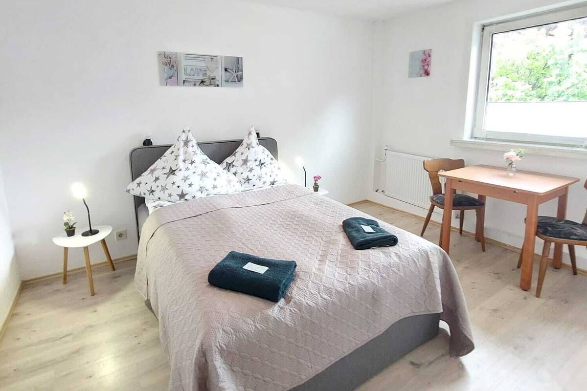 A bedroom with a bed, bedside table, and a desk with chairs.