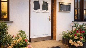 A hotel entrance with a white door, two flower pots with pink and white flowers, and a sign indicating it is a hotel and restaurant. - SILONCE Hotel Bilstein - Lennestadt (Lennestadt)