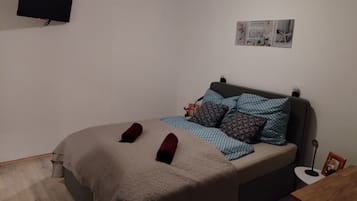 Une chambre à coucher avec un lit, un téléviseur à écran plat fixé au mur et une petite table sur laquelle est posé un cadre photo.