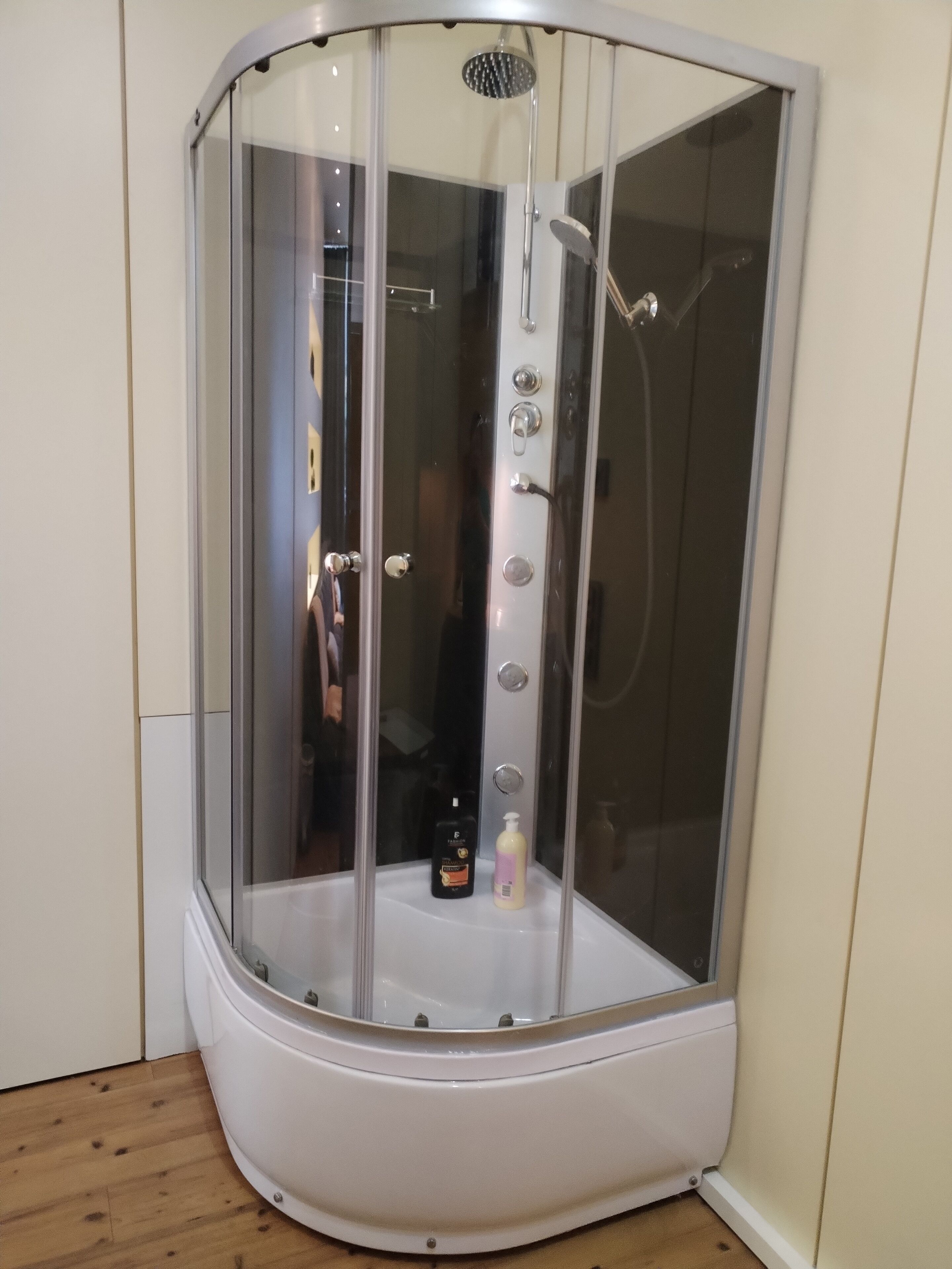 A corner shower enclosure with a glass door, a showerhead, and a control panel.