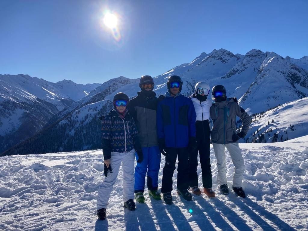 Eine Gruppe von Menschen steht auf einem verschneiten Berg, im Hintergrund ein klarer Himmel und Sonne.