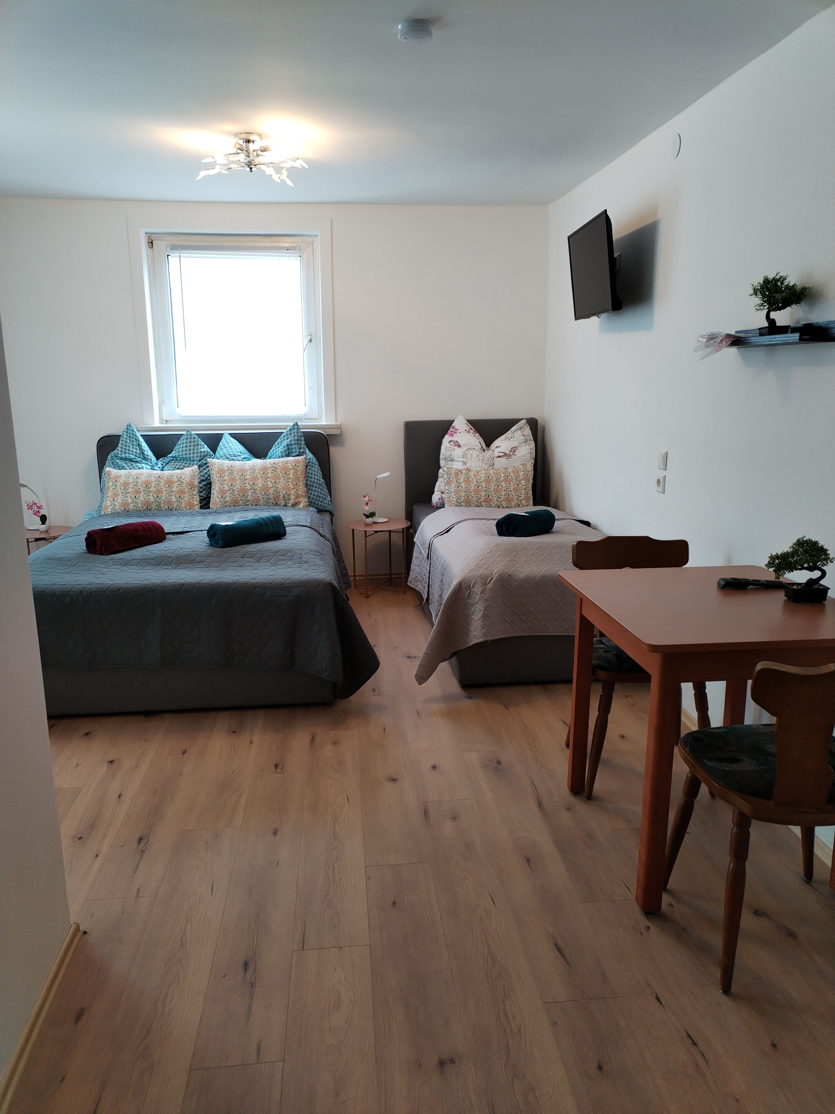 A bedroom with two beds, a wooden floor, a TV on the wall, and a small table with a chair.