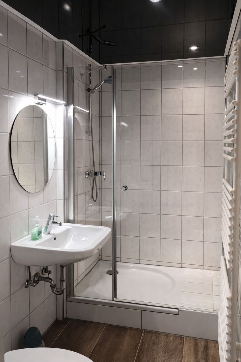 Een moderne badkamer met een douchecabine van glas, een witte wastafel met spiegel en een houten vloer.