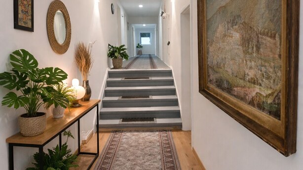 A hallway with a patterned rug, a staircase, and a framed painting on the wall. - SILONCE Hotel Bilstein - Lennestadt (Lennestadt)