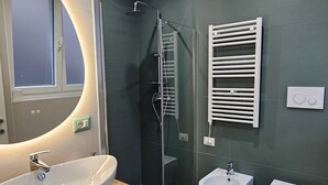 Une salle de bain moderne dotée d'un grand lavabo ovale, d'une douche à parois de verre et de deux bidet sur pied.
