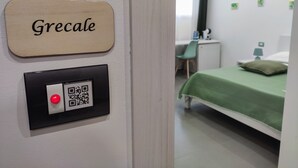 Une pièce avec un lit, un bureau et une chaise. Il y a une pancarte sur le mur où est écrit « Grecale ».