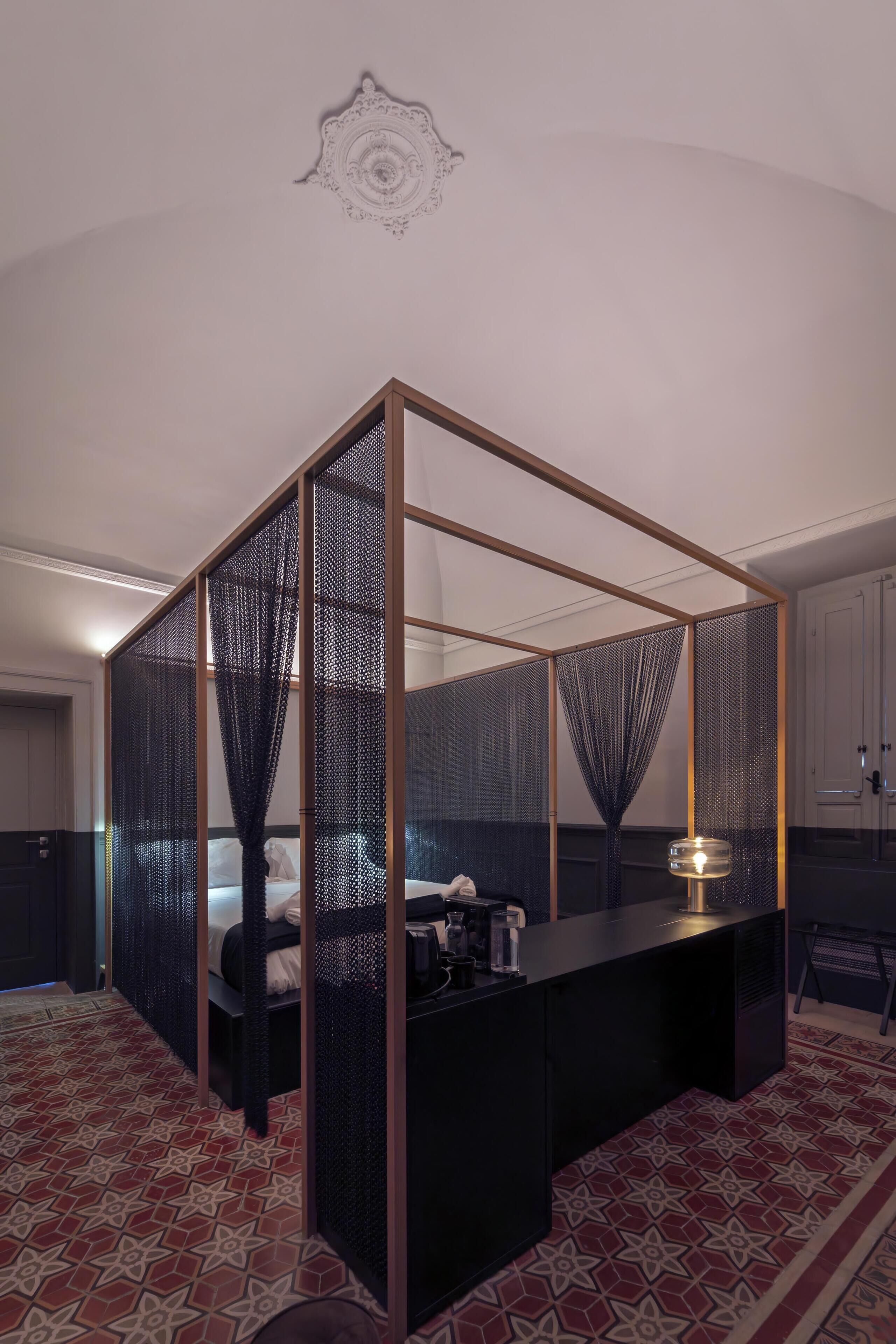 Ein Zimmer mit abgeteiltem Bereich, ausgestattet mit einem Bett, einem kleinen Tisch mit Lampe und einem gemusterten Boden.