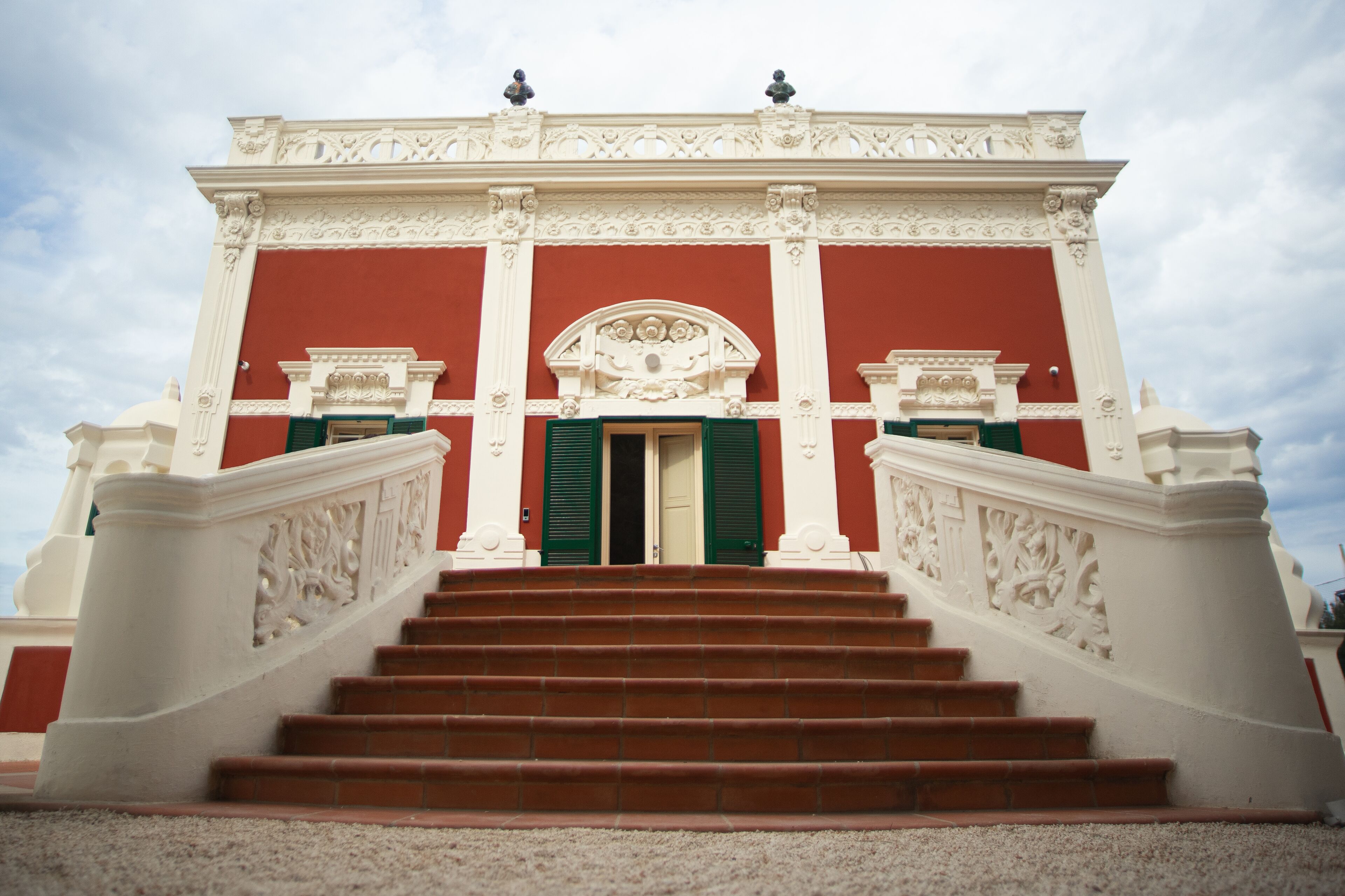 A grand staircase leading to a building with ornate white columns and a red facade.