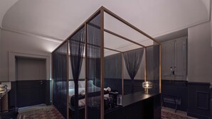 A modern hotel room with a geometric partition, a bed, a desk with a lamp, and a patterned rug.