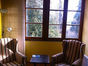A room with two striped armchairs, a small table, and a window with a view of trees.