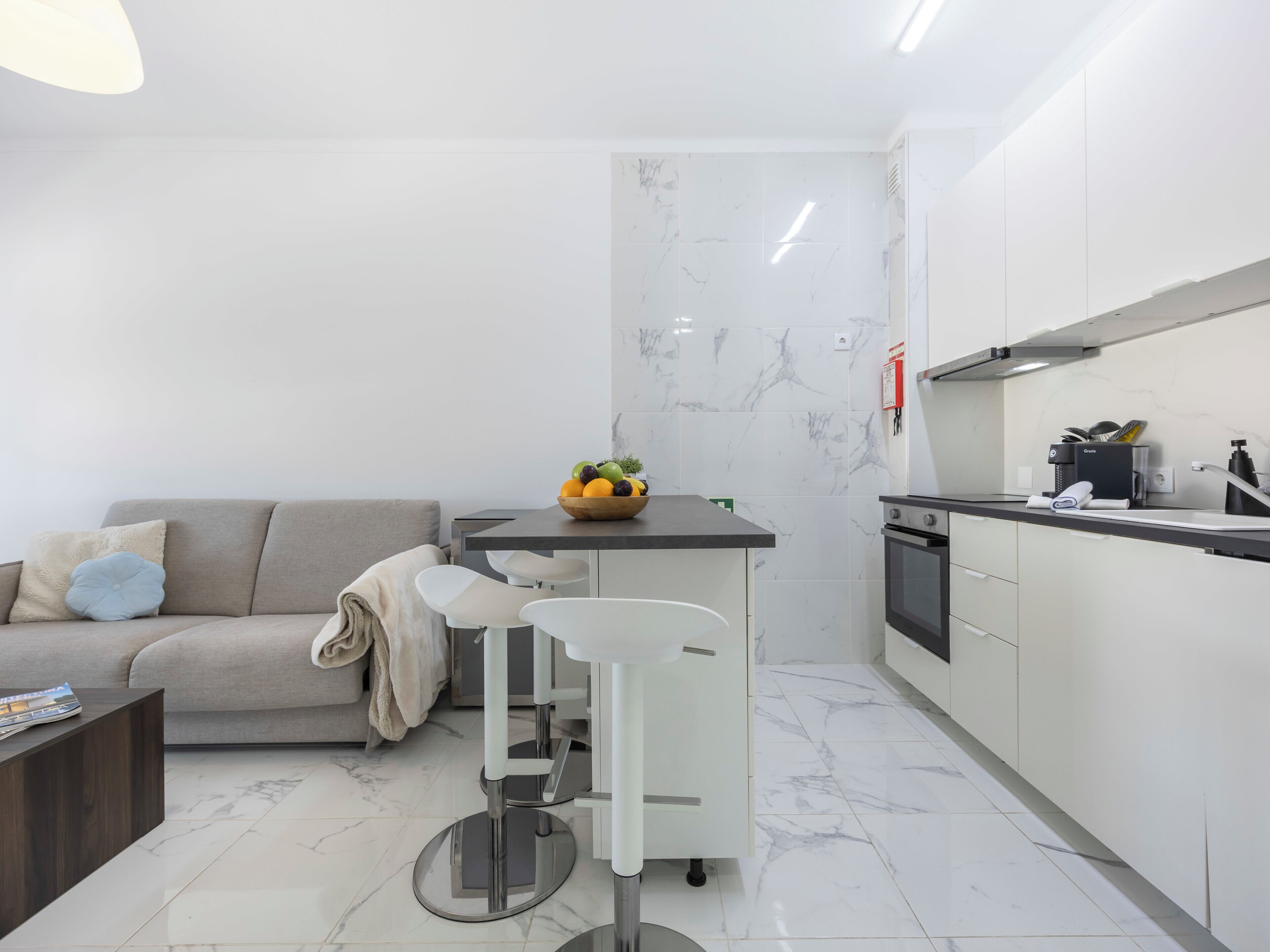 A modern kitchen with white cabinets, a marble backsplash, and a small island with stools.