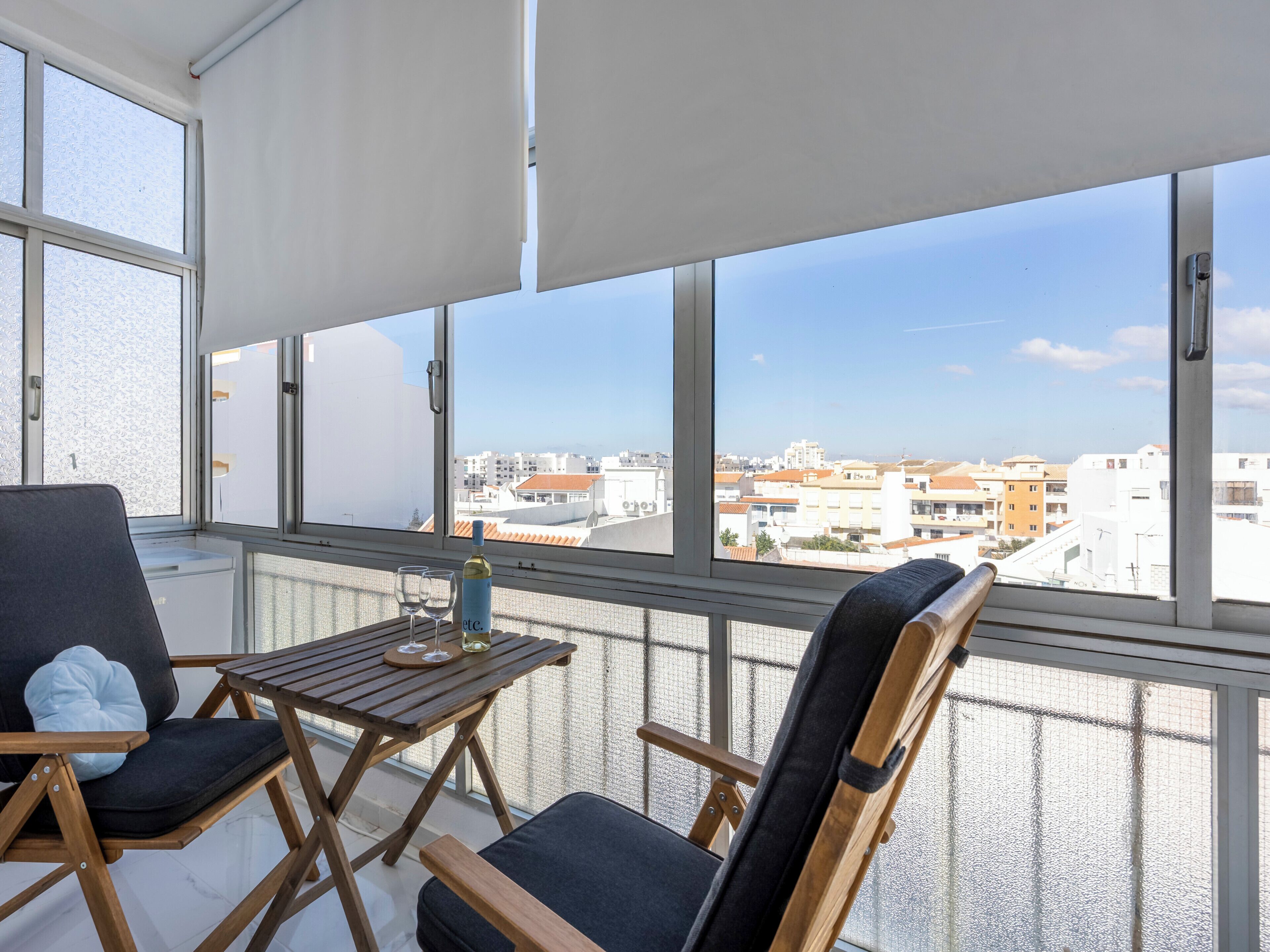 Een balkon met uitzicht op een stadsbeeld, voorzien van een tafel, twee stoelen en een fles wijn.