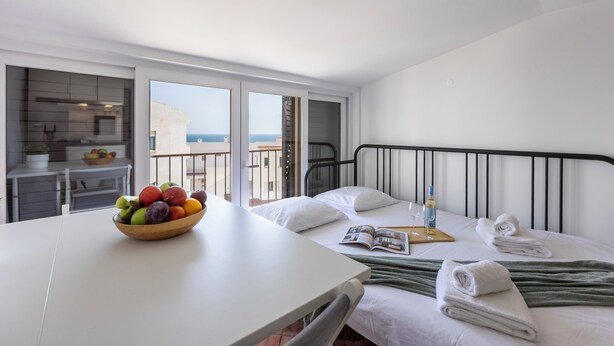 A hotel room with a bed, a dining table with a bowl of fruit, a magazine, and towels.