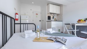A hotel room with a bed, a small kitchenette, a fire extinguisher, and a magazine on the bed.