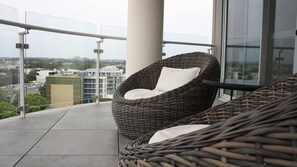 Ein Balkon mit Korbstühlen und Glasgeländer mit Blick auf eine Stadtlandschaft.