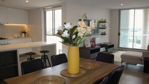 Eine moderne Küche mit Essbereich, mit einem Holztisch, Untersetzern, einer gelben Vase mit Blumen und Blick auf die Stadt durch große Fenster.