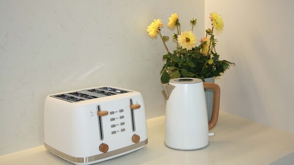 A white toaster with a wooden handle and a white kettle with a wooden handle on a countertop.