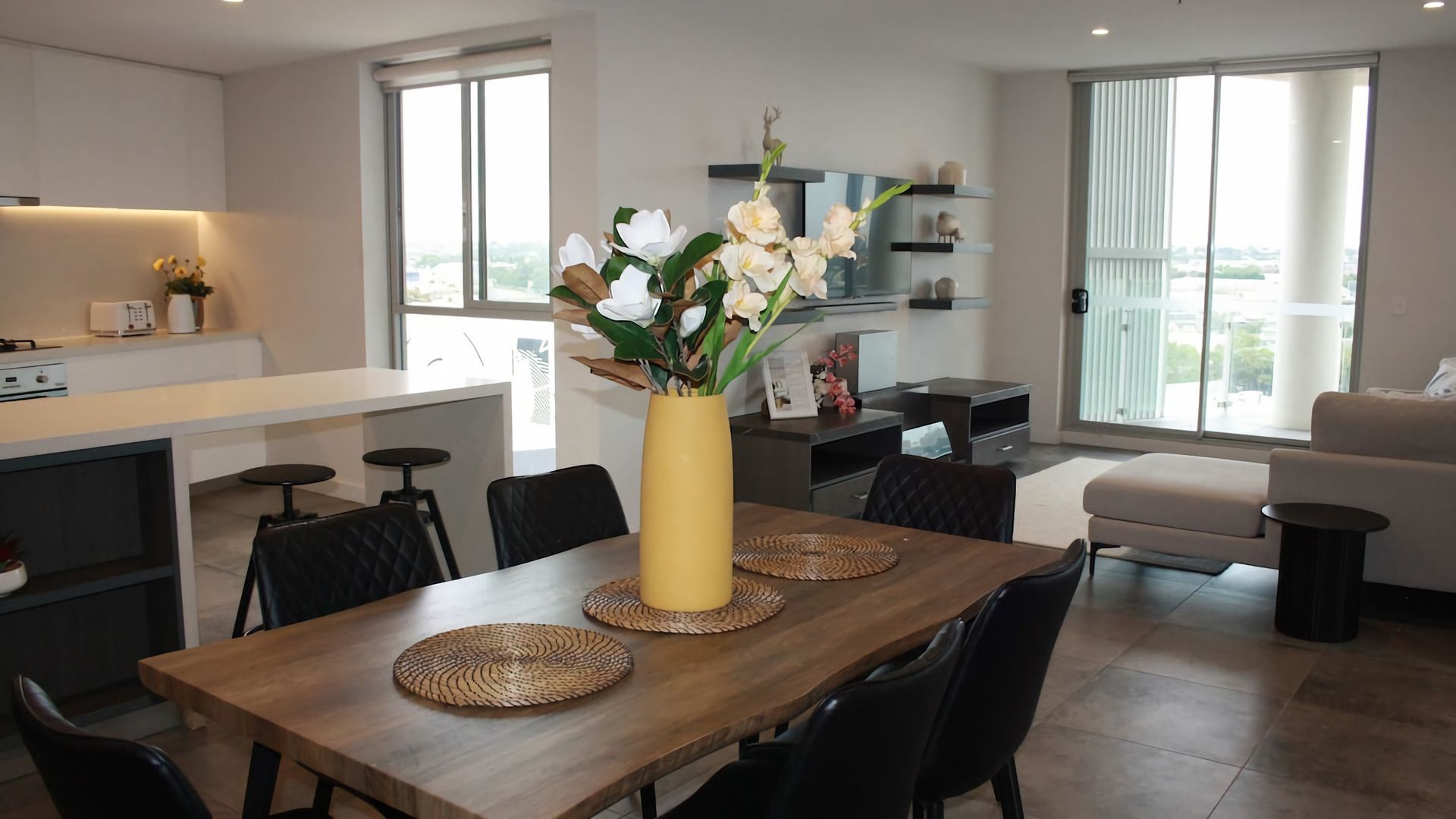 Et moderne køkken med spiseplads, store vinduer og en vase med blomster på bordet.
