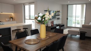 Een moderne keuken met een eethoek, grote ramen en een vaas met bloemen op tafel.