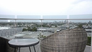 Un balcon offrant une vue sur le paysage urbain, avec une table ronde en osier et une chaise en osier.
